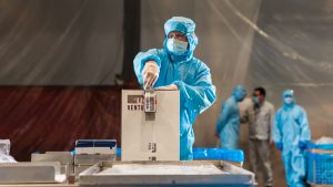 a person in a protective suit and mask seals a box full of breathing aids to be dispatched